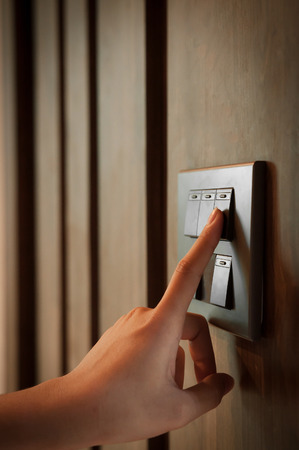 A finger is turning on a grey or black metallic light switch on wooden blackground.の写真素材