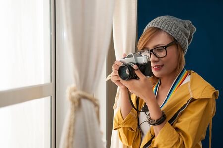 Indoor portrait of Asian pretty woman holding the camera in a house, hipster style, eyeglasses and hat.の写真素材