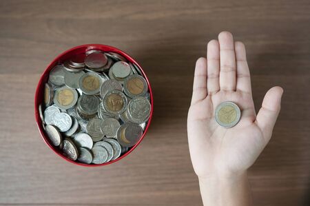 Top view, Saving the money concept, Money in the red bucket on wooden table background, Money coin in a kid hand.の写真素材