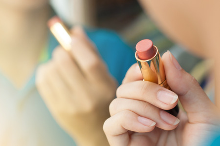 Woman is applying makeup and looking in the mirror. Closeup of red lipstick. Hand of woman is holding lipstick.の写真素材
