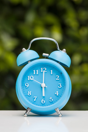 Close up of Blue vintage alarm clock with white floor on green plants and grass background in the...
