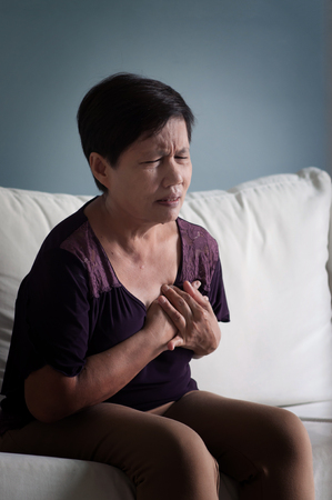 Illness, Ill, exhausted, tired, disease concepts. Senior Asian woman sitting on white sofa and having heart attack.の写真素材