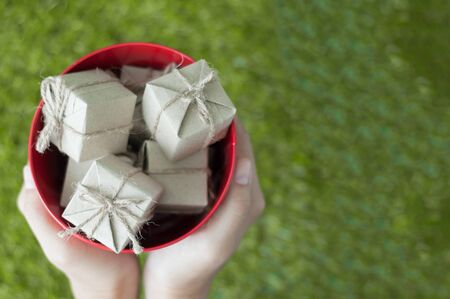 Woman hands holding gift boxes in red bucket on natural background, Christmas and New Year concept. copy space.の写真素材