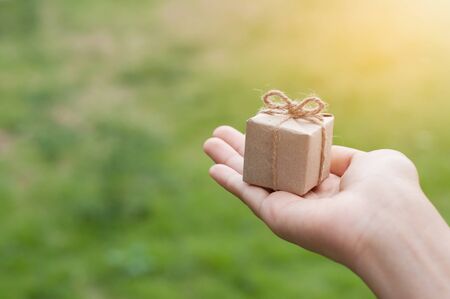 Woman hand holding gift box on natural background at outdoor park, Christmas and New Year concept. copy space.の写真素材