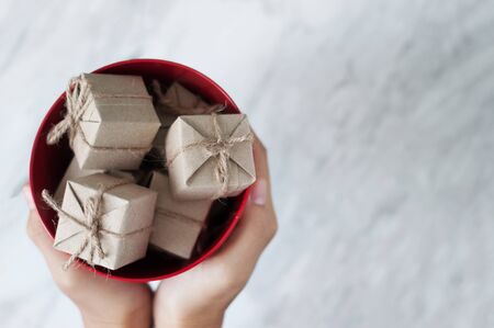 Woman hands holding gift boxes in red bucket on white marble background, Christmas and New Year concept. copy space.の写真素材