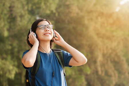 Happiness of Young Asian woman listening music with headphone in nature.Beautiful glasses girl closed her eyes and smiling with fresh air.の写真素材