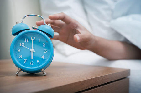 Woman hand reaching out bed for retro alarm clock. Early morning.の写真素材