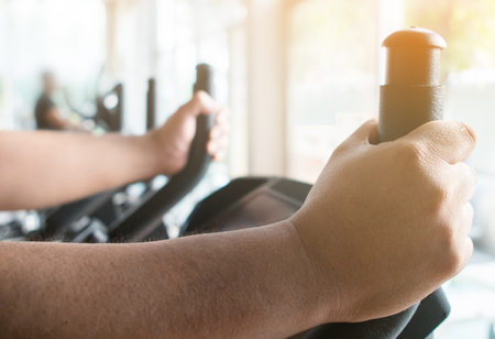 Close up fat man hands on exercise bike, cycling, stationary exercising.の写真素材