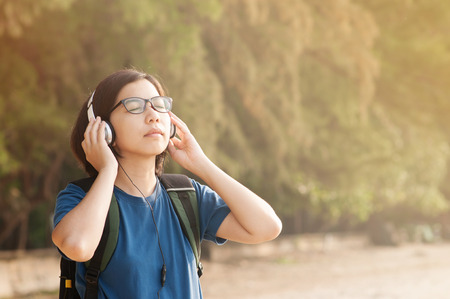 Happiness of Young Asian woman listening music with headphone in nature.
Beautiful  glasses girl closed her eyes and breathing fresh air.の写真素材