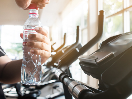 Close up fat man hands opening bottle of water on exercise bike, cycling, stationary exercising. Tired.の写真素材