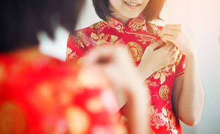Chinese new year. Asian woman with cheongsam looking  to mirror. Girl is smiling. Get dress.の写真素材