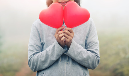 Valentine's concept. Asian woman holding red hearts on fog and grass field background. Copy space. Vintage or retro color. winter.の写真素材