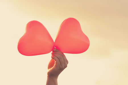 Valentine's concept. Close up hand holding red hearts over sky with sunlight background. Copy space.の写真素材