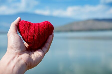 Valentine's concept. Close up hand holding red hearts on blue sky  and sea background. Copy space.の写真素材