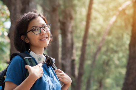 Asian glasses woman hiker with backpack and headphone smiling on nature background.の写真素材