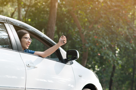 Asian traveler woman having fun and taking photo from inside the car with cell-phone or smart-phone in nature.の写真素材