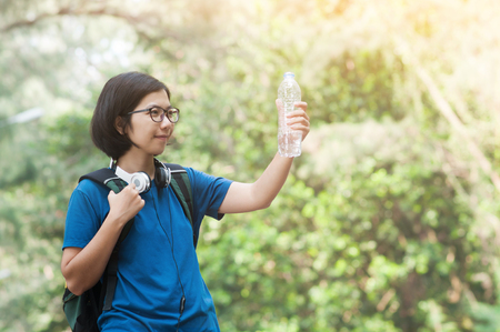 Asian woman hiker with backpack wear headphone holding bottle of water on nature background. copy space.の写真素材