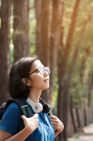 Asian glasses woman hiker with backpack breathing nature fresh air. Beautiful girl with  headphone smiling on nature background.の写真素材