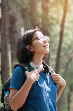 Asian glasses woman hiker with backpack breathing nature fresh air. Beautiful girl with  headphone smiling on nature background.の写真素材