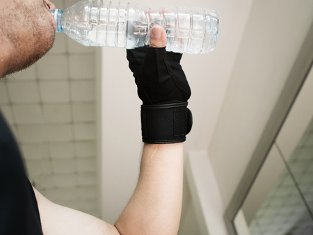 Close up man hands wear gloves holding bottle of water at a gym. People dinking water. Tired, thirstily.の写真素材