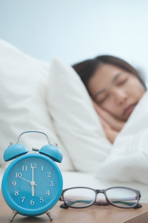 Relaxed of young Asian woman sleeping on bed in winter.  Retro alarm clock and glasses on foreground.の写真素材