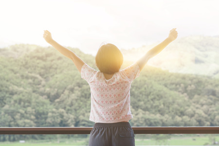 Asian woman standing at balcony and looking on the landscape. Rear view.  Raised up hands. Relaxations, Happiness, Freedom.の写真素材