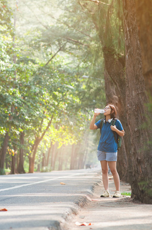 Asian woman hiker with backpack resting and drinking water with sunlight on nature background. copy space.の写真素材