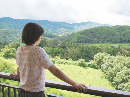 Asian woman standing at balcony and looking on the landscape. Rear view.の写真素材