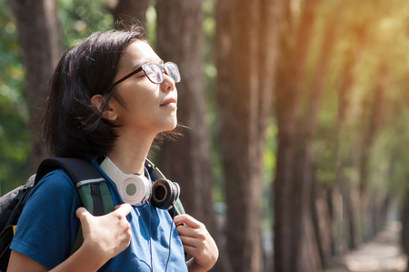 Asian glasses woman hiker with backpack breathing nature fresh air. Beautiful girl with  headphone smiling on nature background.の写真素材