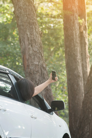 Asian traveler woman having fun and taking photo from inside the car with cell-phone or smart-phone in nature.の写真素材