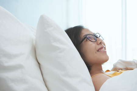 Happiness of young Asian glasses woman smiling and lying on bed in the morning. Copy space.の写真素材