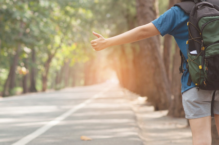 Woman hitchhiker with backpack sign thumb up on highway road with sunlight on nature background.の写真素材