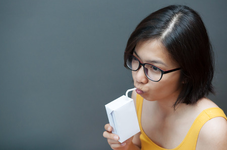 Asian glasses woman drinking milk with copy space.  Milk carton.の写真素材