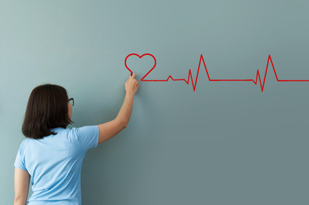 Woman drawing  heartbeat with red chalk on wall. Copy space. wellness concept.の写真素材