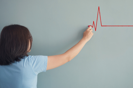 Woman drawing  heartbeat with red chalk on wall. Copy space. wellness concept.の写真素材