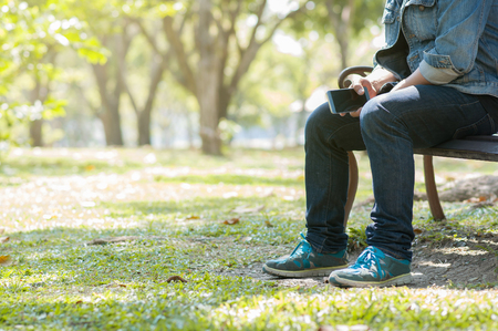 Man sitting with  mobile phone at the natural park. Male in blue jean and jacket resting or relaxing with copy space.の写真素材