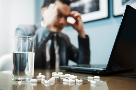 Illness, stressed, tired, exhausted, pain from overworked concepts. Asian Businessman has headache from migraine. Pills with water on foreground.の写真素材