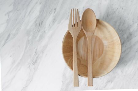 Wooden spoon, fork and bowl on white marble background. Copy space.
