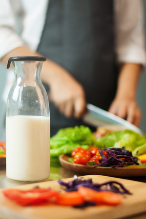Milk in bottle with woman cooking and vegetables.の写真素材