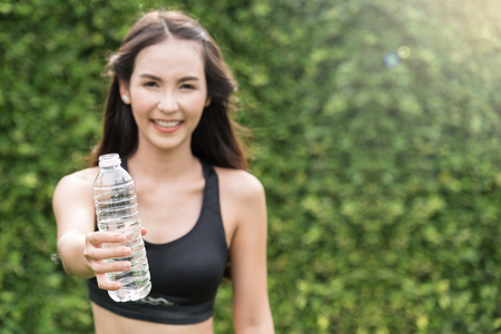 Asian woman in sportswear holding bottle of water on natural background. freshness, happiness, relaxing and smiling.の写真素材