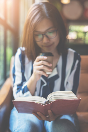 Focus on book. Relaxed Asian Woman holding a cup of coffee and reading a book.の写真素材
