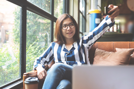 Relaxed Asian Woman using cell phone. Happiness eyeglasses girl smiling.の写真素材