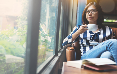Relaxed Asian Woman holding a cup of hot coffee. Happiness eyeglasses girl smiling.の写真素材