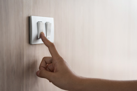Close up hand turning on or off on grey light switch with wooden background. Copy space.
