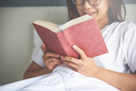 Asian glasses woman reading a book on her bed.の写真素材
