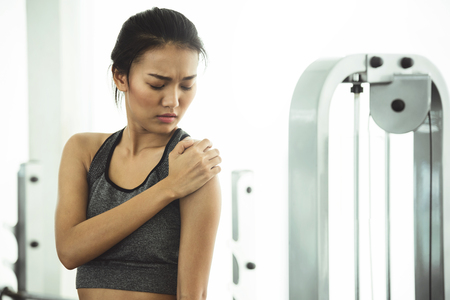 Asian woman in sportswear having shoulder pain at the gym.の写真素材