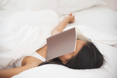 Relaxed Asian girl sleeping on her bed with a book on her face.の写真素材