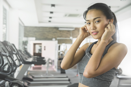 Relaxed Asian woman in sportswear listening to the music with her cell phone at the gym.の写真素材