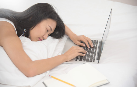 Asian girl sleeping with laptop on her bed. Girl listening to the music with earphones.の写真素材