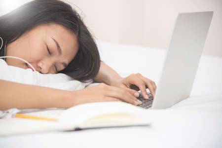 Asian girl sleeping with laptop on her bed. Girl listening to the music with earphones.の写真素材